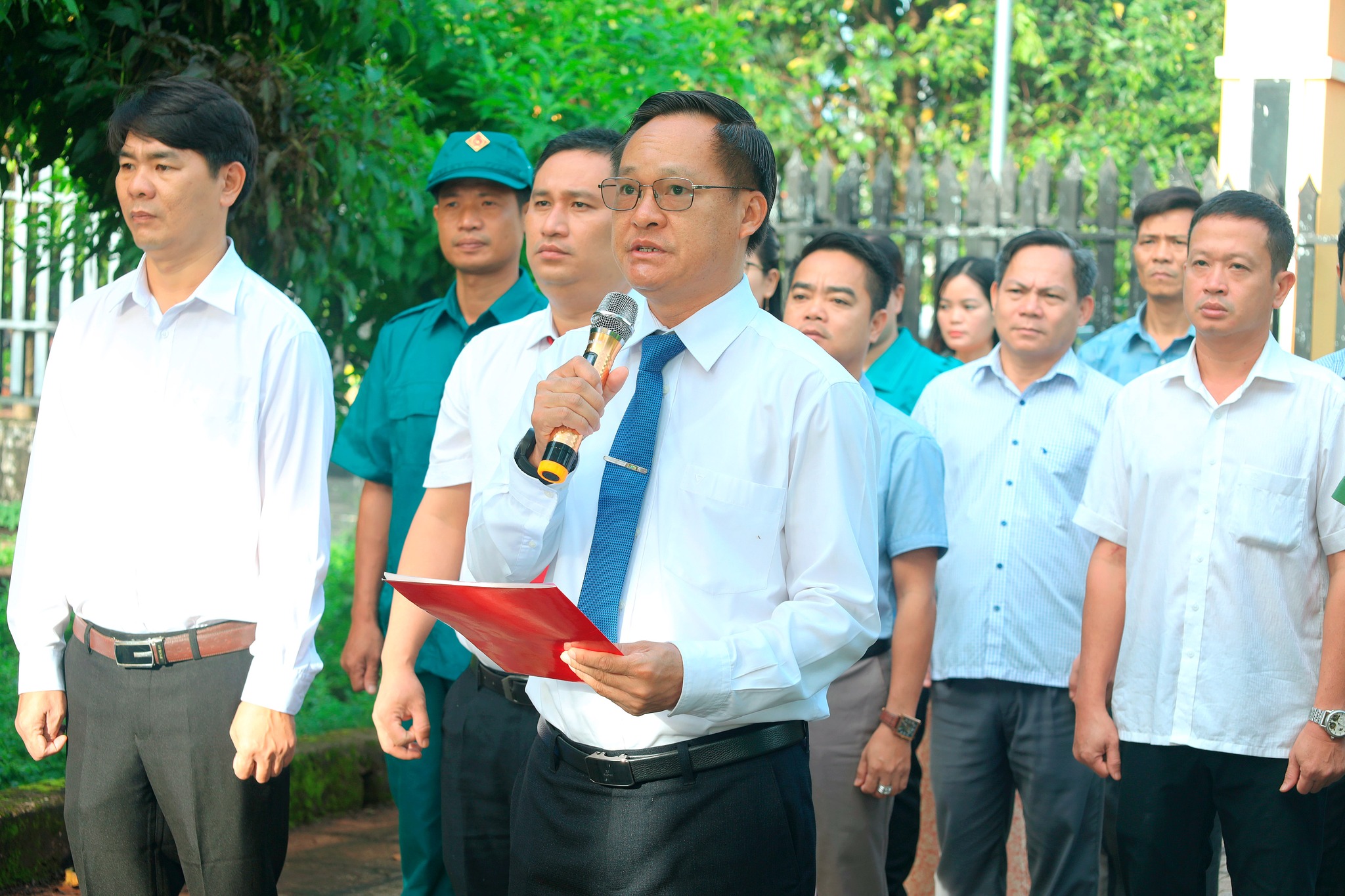 ''A person holding a microphone and standing in front of a group of people
Description automatically generated''