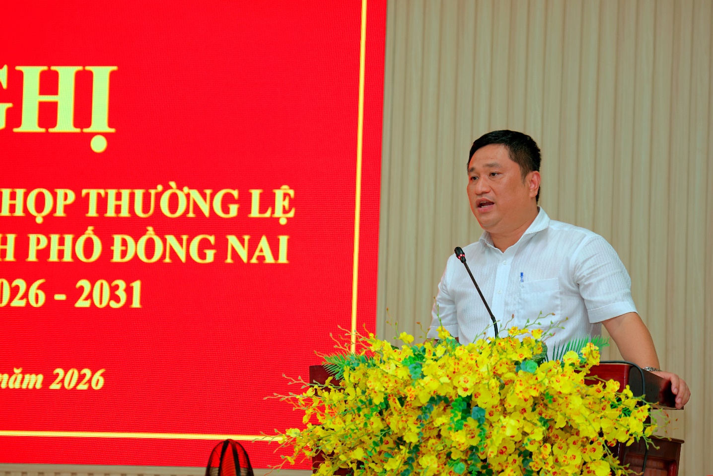 'A person standing at a podium with yellow flowers
Description automatically generated'