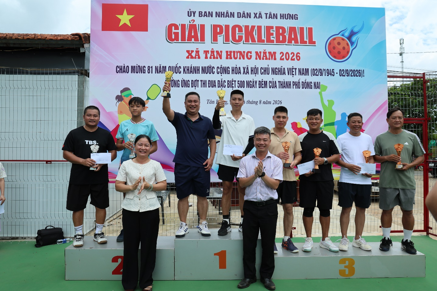 A group of people standing on a podium holding trophies
Description automatically generated